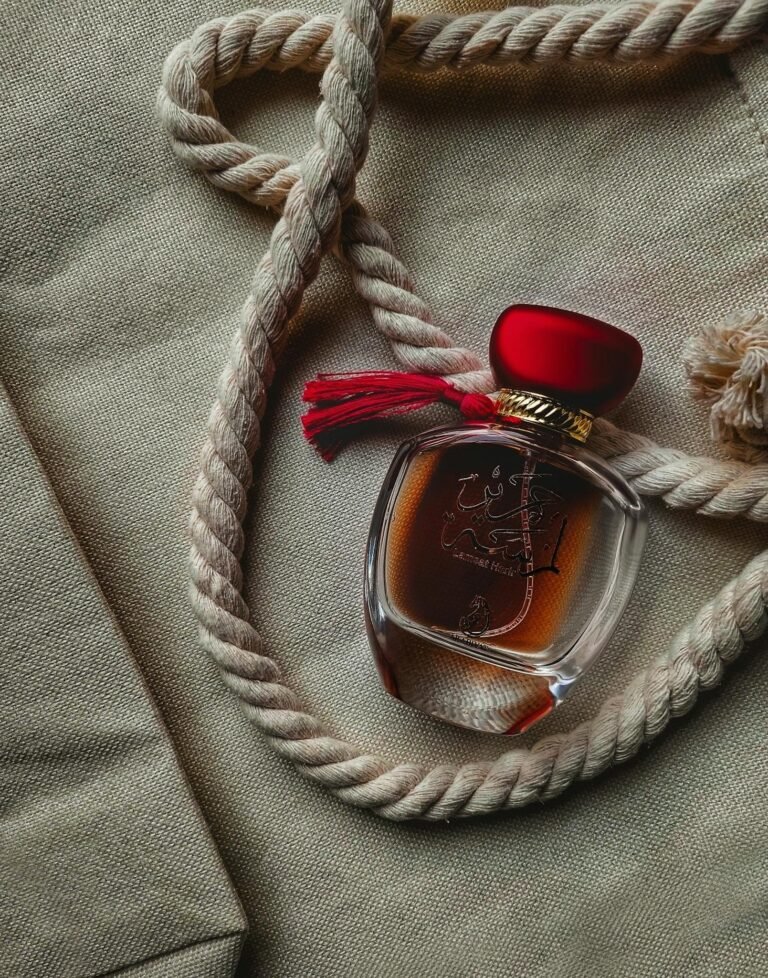 Elegant perfume bottle with red cap placed on nautical rope and textured fabric background.