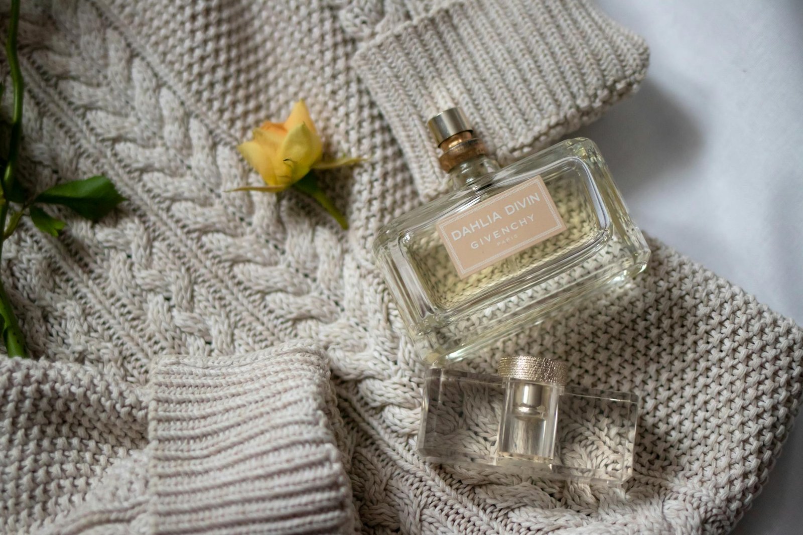 Luxurious Givenchy perfume bottles with a yellow rose on a knitted sweater, exuding elegance.